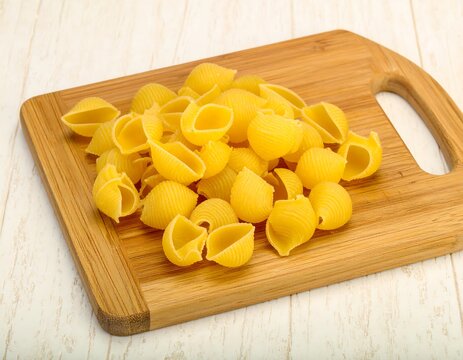 Pile of pasta shells on a wooden cutting board - Powered by Adobe