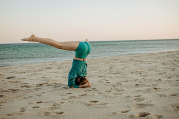Fototapeta premium Woman performing Sirsasana (headstand) on the beach during sunrise. Yoga practice by the ocean for strength, balance, and mental focus in a calm, natural environment