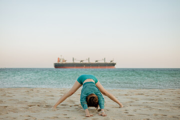 Young woman practicing Prasarita Padottanasana on a sandy beach by the ocean. Morning yoga for...