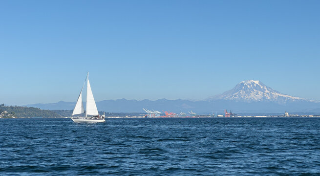 Isolated sailboat sailing in Puget Sound's Commencement Bay with the port of Tacoma and Mount Rainier in the distance. 