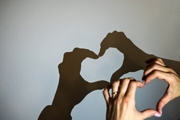 mani che formano un cuore con le ombre sul muro