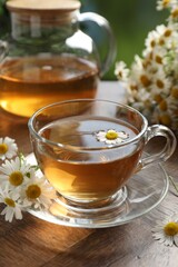 Aromatic tea in glass cup and chamomile flowers on wooden table, closeup