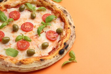 Delicious pizza with tomatoes, basil and olives on orange background, closeup. Space for text