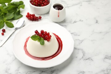 Delicious panna cotta with red currants, sauce and mint on white marble table, closeup