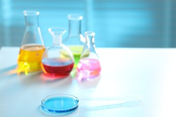 Laboratory glassware with different samples on light table, closeup. Space for text