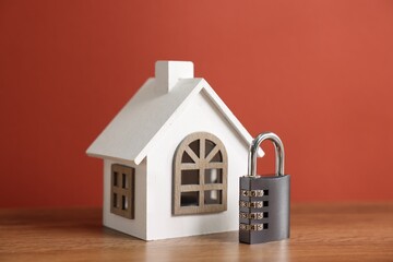 Home security. House model and padlock on wooden table against red background