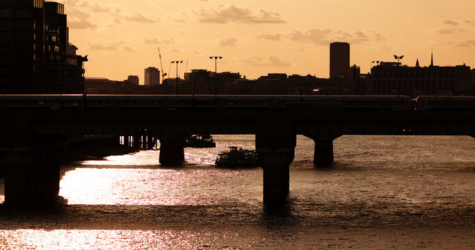 Train crossing a bridge over River Thames with a boat passing underneath at sunset in London, United Kingdom