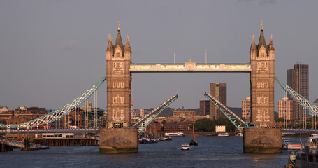Tower Bridge opening in London with a boat passing by on River Thames during sunset