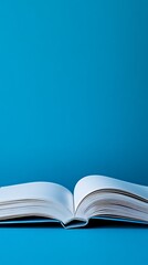 An open book with blank pages is placed on a solid blue surface under bright lighting conditions studio shot
