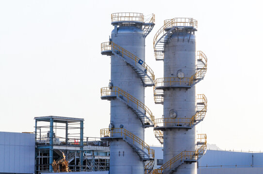 Two tall industrial process towers with spiral staircases stand at a stand-alone electric battery manufacturing plant under construction, representing essential facility infrastructure components