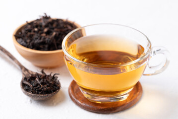 Black tea in cup glass with dried tea leaves on white background, Healthy herbal hot drink