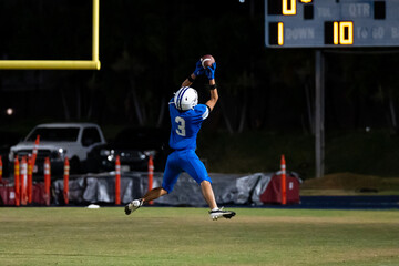 Football player leaps mid-air under goalpost for critical catch in night game—dynamic action shot...