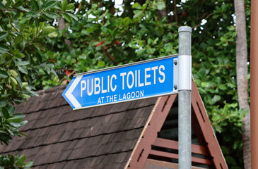 Public Toilets At The Lagoon sign attached to a metal pole in a park with tropical trees