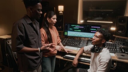 Zoom out shot of young musicians high five while working on new music in recording studio and producing tracks via mixing console