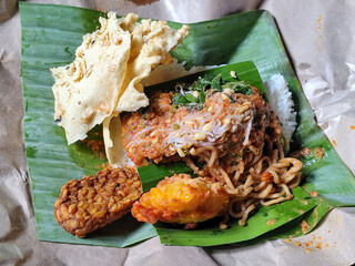 Nasi pecel or sego pecel is a typical Javanese Indonesian rice dish served with pecel sauce, which can be added with vegetables, peyek, tempeh and other side dishes. With a banana leaf base.
