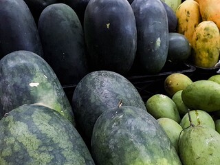 Variety of ripe watermelons, mangoes, and papayas displayed at a market, showcasing fresh, healthy produce ready for consumption.