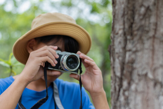 Asian teen boy in blue t-shirt and wears hat and holding camera for exploring the forest on a sunny day, enjoying outdoor adventure and wildlife observation. - Powered by Adobe