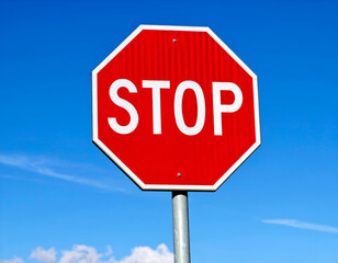 Bright red octagonal stop sign against a clear blue sky, symbolizing traffic safety and the need to halt.
