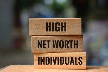 Wooden block with the words 'high, net worth, individuals' on an blurred background. The concept of wealth and finance.