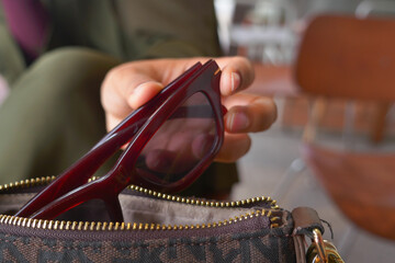 Stylish sunglasses being placed in a handbag after use
