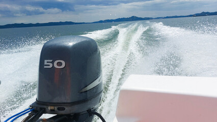Powerful outboard motor propelling boat, creating foamy wake on lake, with distant hills under...