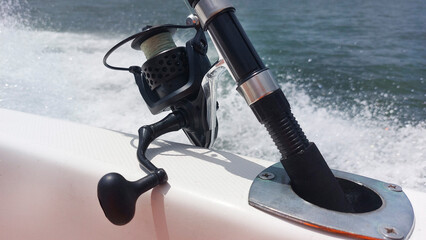 Fishing rod secured to a boat, racing across the water surface, generating dynamic waves and lively...