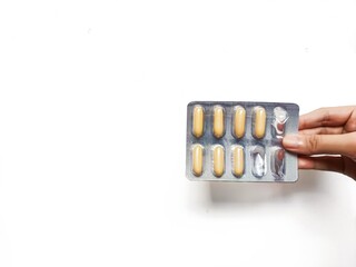 Hand holding a blister pack of yellow capsule pills against a white background. Healthcare and...