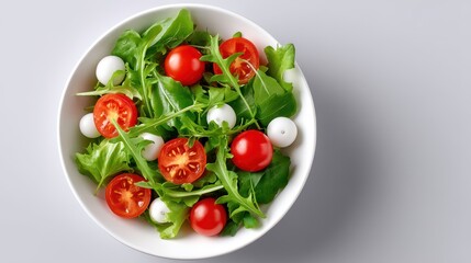 Fresh green salad with cherry tomatoes and mozzarella balls in a white bowl.