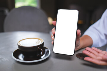 Mockup image of a woman holding and showing a mobile phone with blank white screen in cafe