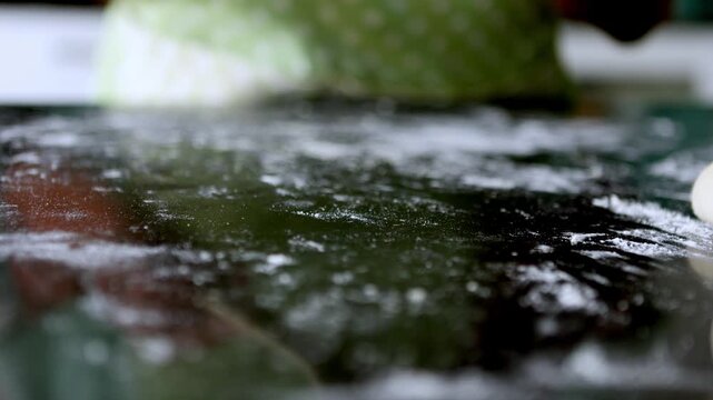 Baker using wooden spatula to flatten dough ball on floured surface