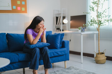 Young woman suffering from depression, sitting on sofa in living room at home