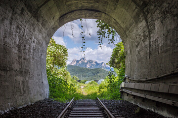 Tunnel Framing Snow Covered Mountain Peaks With Lush Green Vegetation In Foreground Photo