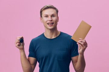 smiling young man hold car keys envelope wear casual blue t-shirt isolated pink background concept...