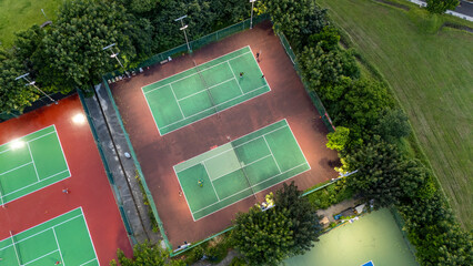 Aerial View of Tennis Courts Lit Up for Night Play Showing Green Surfaces and Red Accents