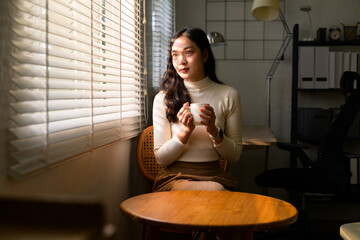Young Asian businesswoman relaxing with coffee cup and looking outside window blinds in modern office