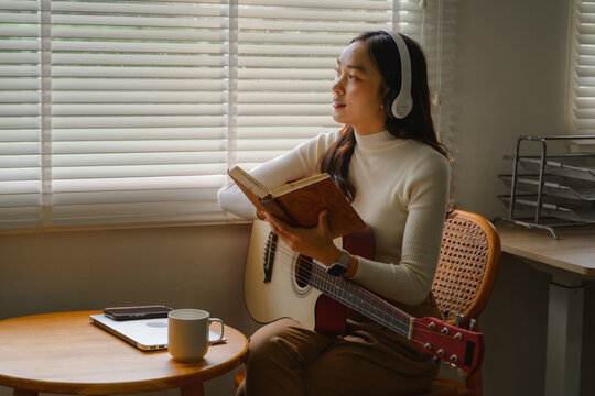 Young woman composing music reading a book and holding acoustic guitar
