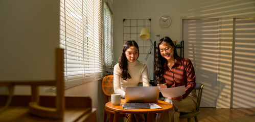 Two businesswomen working together on a laptop in a sunlit home office