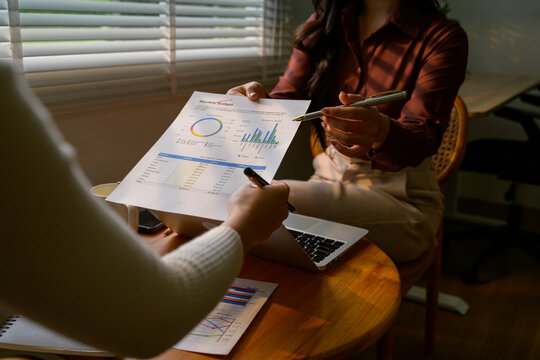 Businesswomen analyzing financial monthly budget report document with charts and graphs using laptop computer and pen