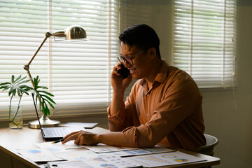 Asian businessman talking on phone and analyzing financial charts at home office