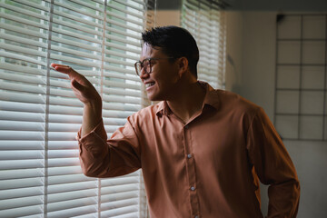 Asian businessman looking out the window through blinds