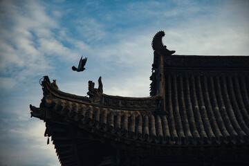 Historic Chinese temple rooftops with intricate decorations and a bird in flight during twilight