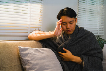 Obraz premium Sick young man suffering from headache while sitting on sofa at home