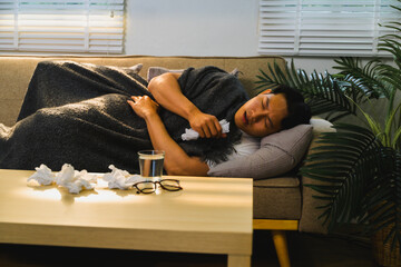 Sick asian man lying on sofa, holding tissue and suffering from cold or flu