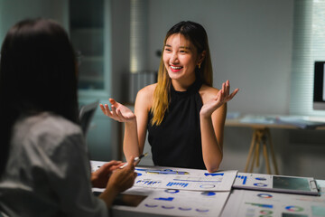 Fototapeta premium Asian businesswomen discussing and working late together using charts and graphs