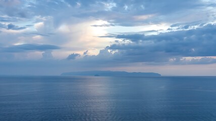Fototapeta premium Serene ocean vista with dramatic clouds and sunlight breaking through reflecting on calm water surface