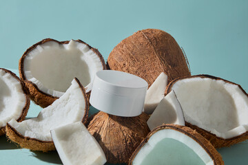 Coconuts cut open with a cream jar placed inside decorated on blue background. This creative photo links coconut’s freshness with nourishing cosmetic products for skin and hair.