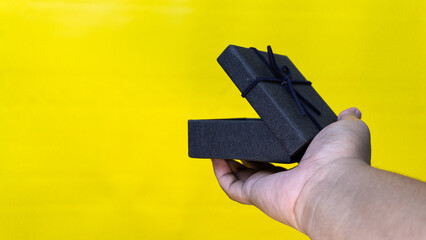 Open black gift box held in right hand with yellow background, perfect for surprise, present,...