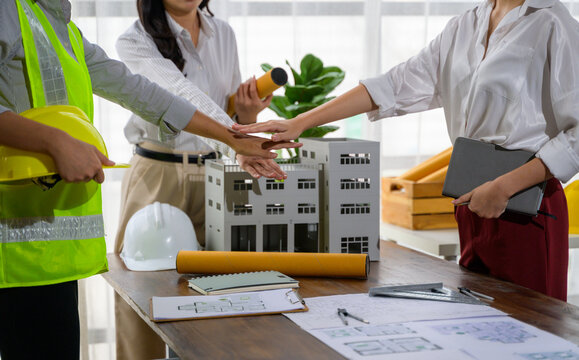 Architects joining hands over building model celebrating successful project