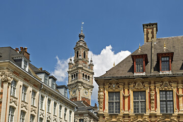 Obraz premium The Chamber of Commerce Belfry in Lille, Its ornate tower rises above the rooftops of the Grand Place, featuring red brick and white stone detailing, arched windows, and a decorative spire. 
