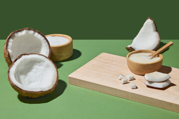 Creative setup of coconuts and a wooden bowl with scrub on green background. The arrangement reflects coconut as a raw yet refined element in natural cosmetic care. Space for display product